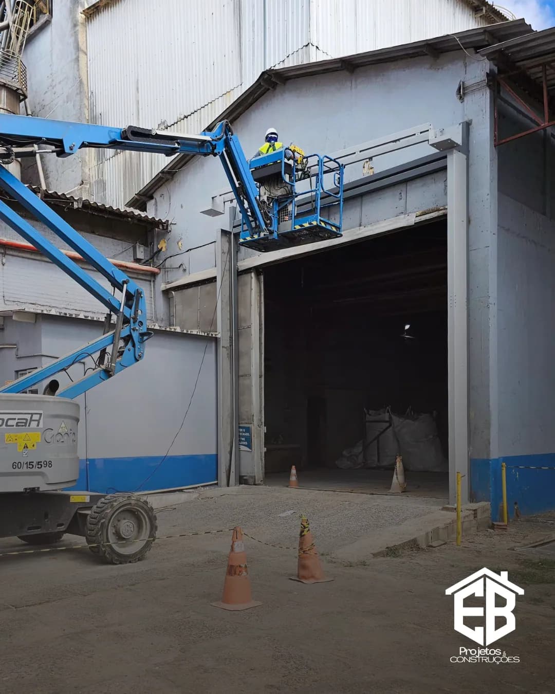 Plataforma articulada posicionada na entrada do galpão para serviço na fachada