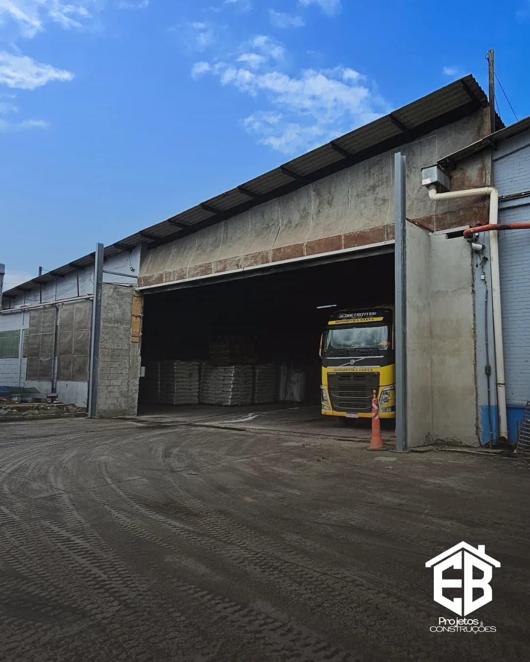 Vista externa do galpão industrial com acesso de veículos durante a obra